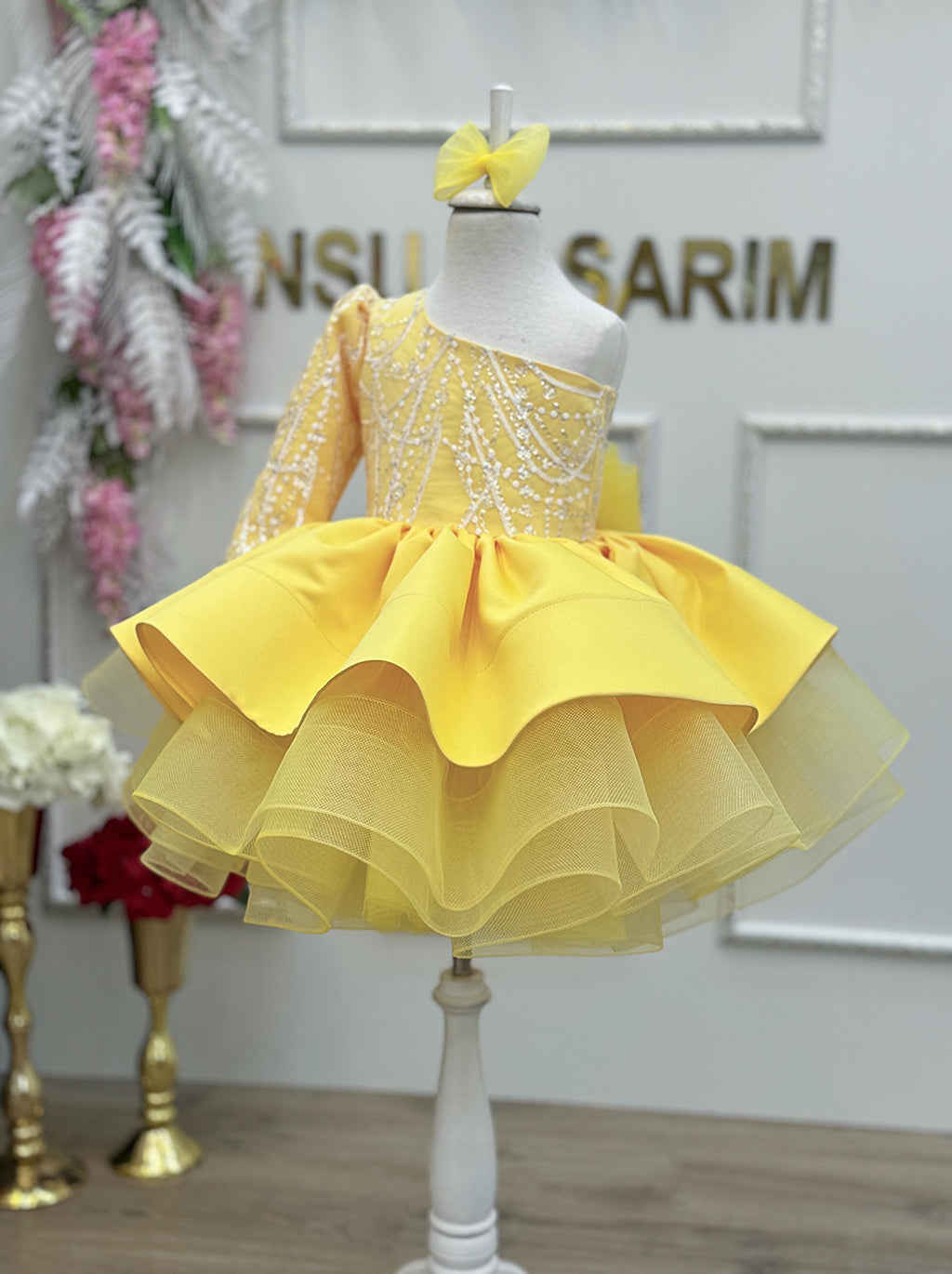 One-year-old girl in a yellow one-shoulder tulle first birthday dress with a shiny silver lace bodice.