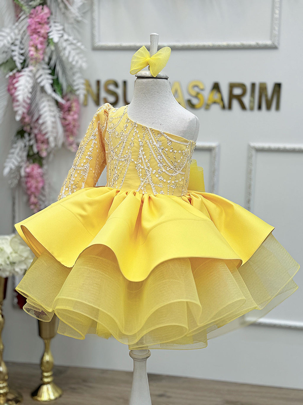 Handmade one-shoulder first birthday dress with a silver lace top and yellow tulle skirt displayed on a mannequin.