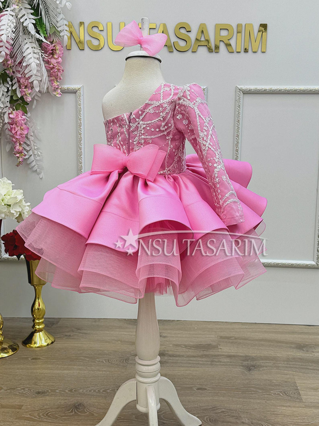 Little girl celebrating her first birthday in a pink one shoulder dress with a fluffy tulle skirt and matching headband.