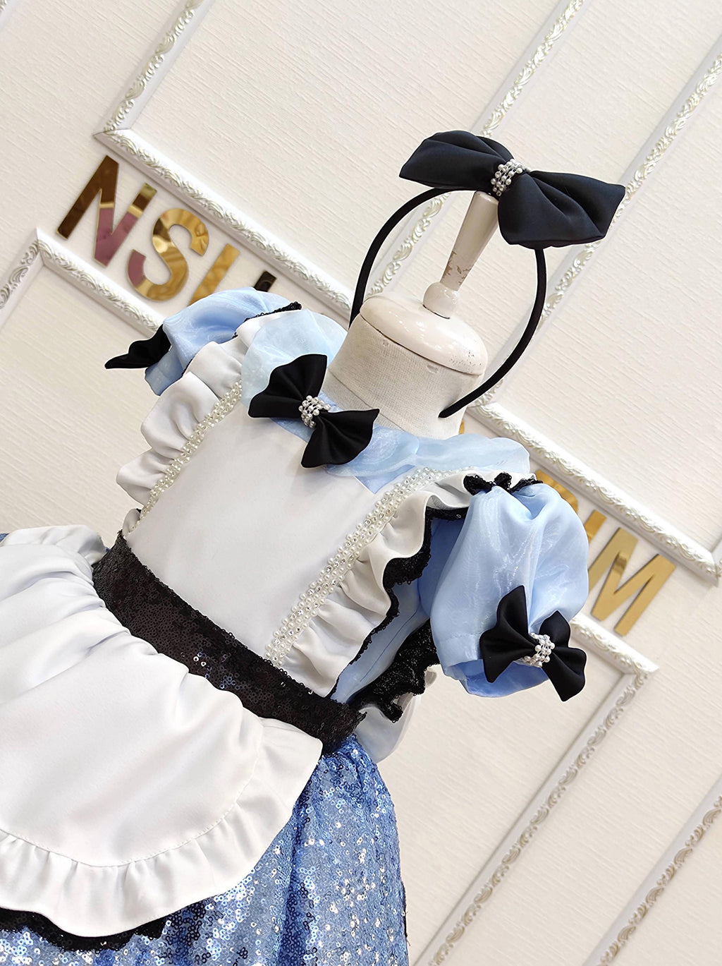 Disney Alice dress or costume . Blue and white first birthday dress outfit displayed on a hanger with matching black bow accessories.